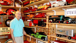 Bill Bangert of Newark stands in his garage next to a portion of his pressed-steel toy car models big enough to be sat on by young children. These car models disappeared in the late 1950s. 